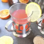 Warm Christmas punch served in a stainless steel glass cup with a slice of lemon.