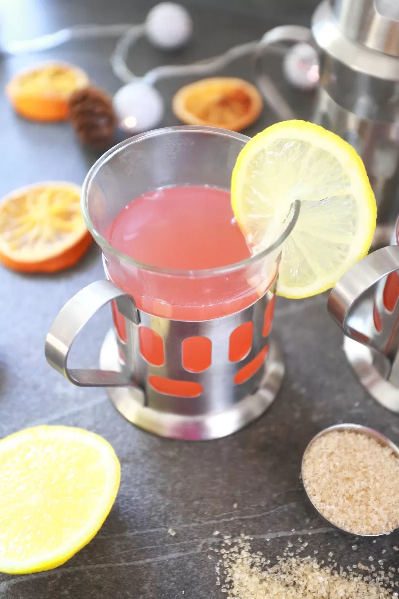 Warm Christmas punch served in a stainless steel glass cup with a slice of lemon.