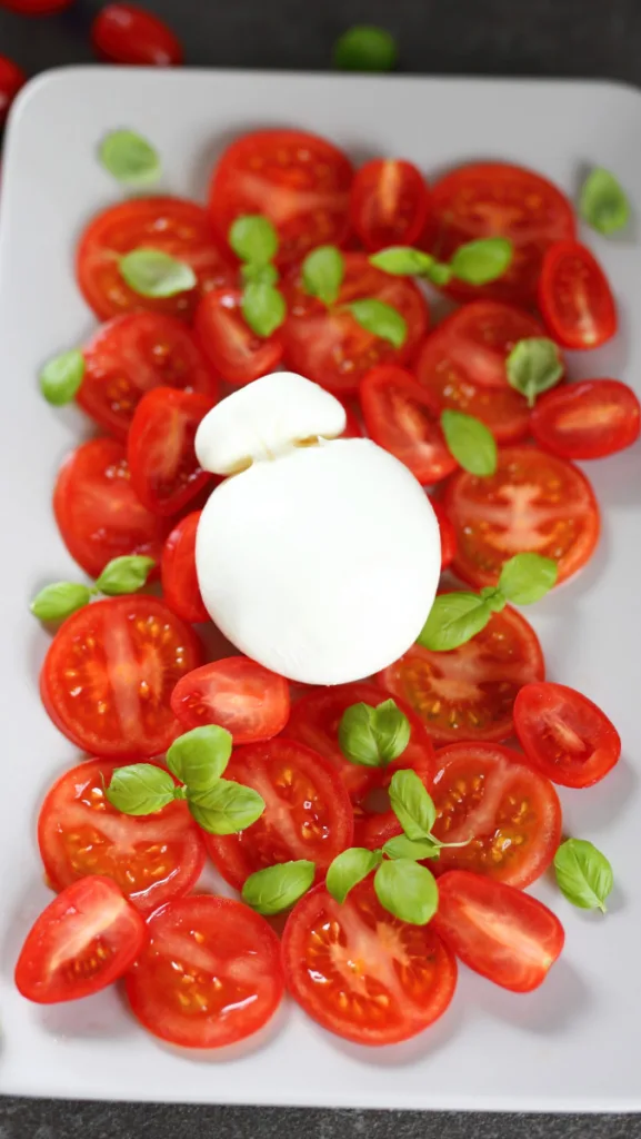 Sliced tomatoes on a platter topped with Burrata Cheese ball and basil leaves.