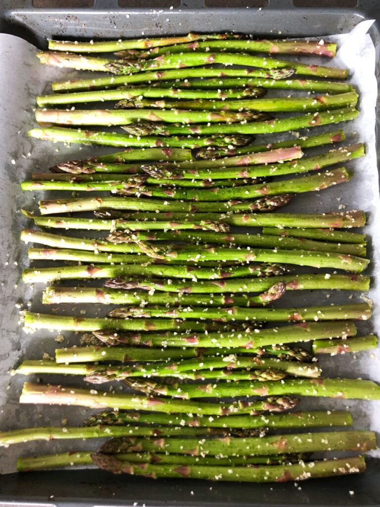 Seasoned asparagus on baking sheet ready for roasting.