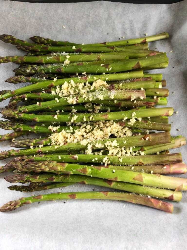 Asparagus on baking sheet with garlic and seasonings.