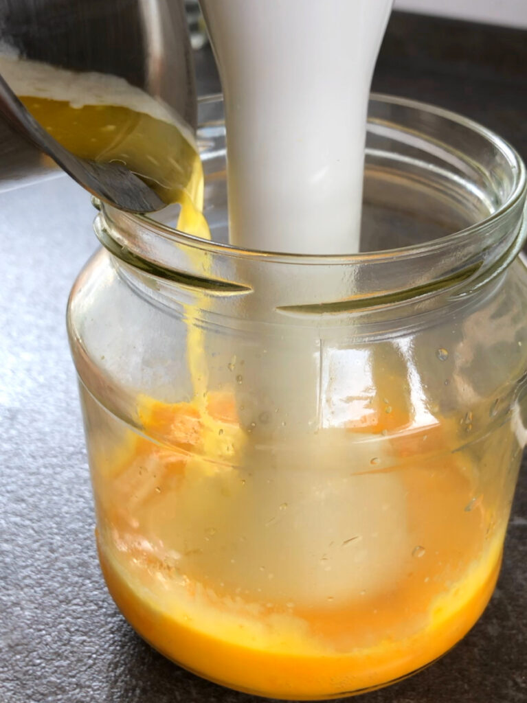 Blending hollandaise sauce together with immersion blender in a jar.