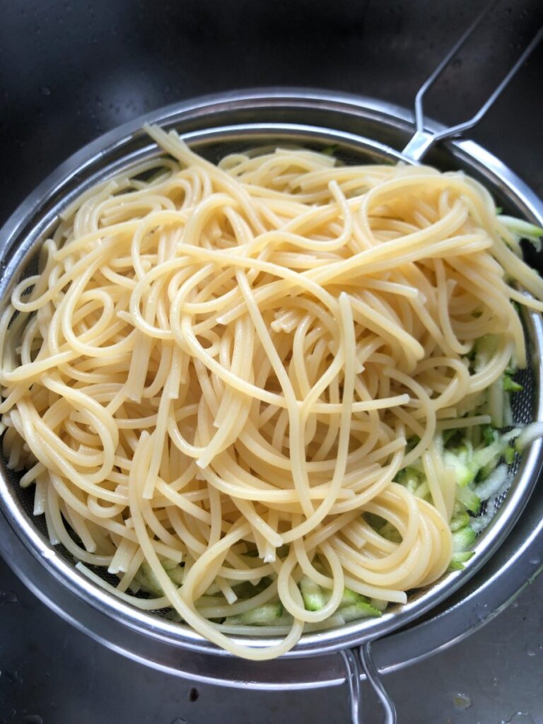 Cooked spaghetti tossed on shredded zucchini.