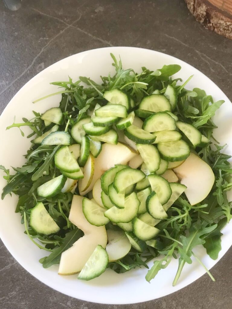 Arugula with sliced pear and cucumber in a bowl