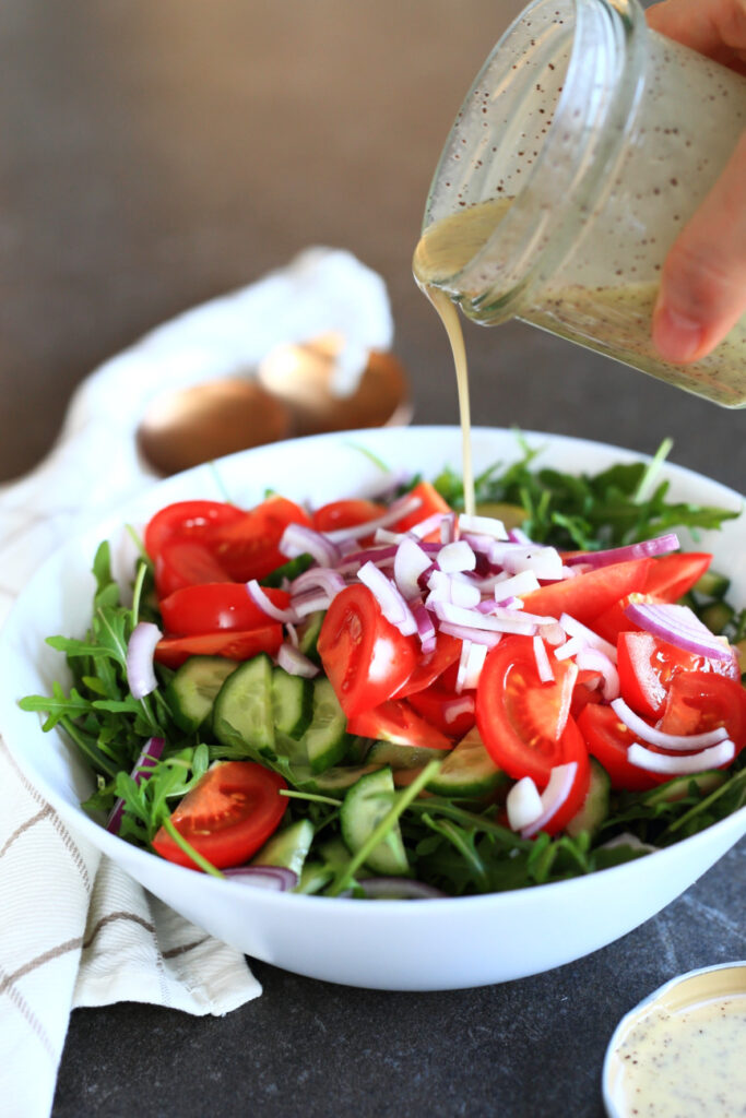 Arugula pear salad with poppy seed salad dressing poured from a jar