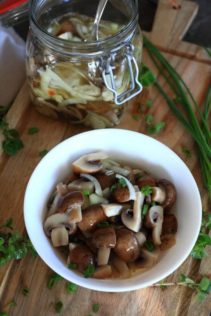 Marinated mushrooms in a bowl surrounded by herbs